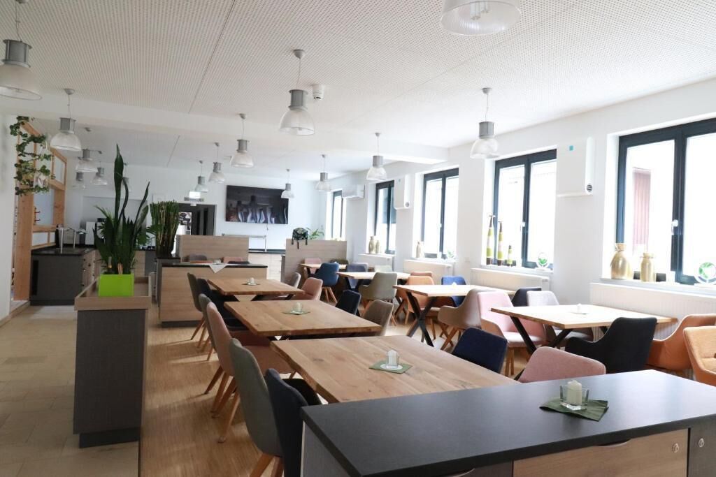 A modern dining area with multiple tables and chairs, large windows, and pendant lighting.
