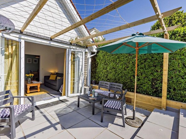 An outdoor patio with a table and chairs, a green umbrella, and a wooden pergola. - 2 Bed in Bude (oc-82163) (Bude)