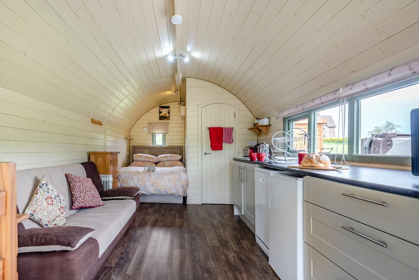 Un intérieur chaleureux avec un lit, un canapé, un coin cuisine doté d’une fenêtre et des murs en bois.