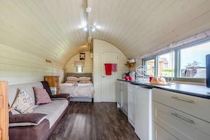 A cozy interior with a bed, a sofa, a kitchen area with a window, and wooden walls.