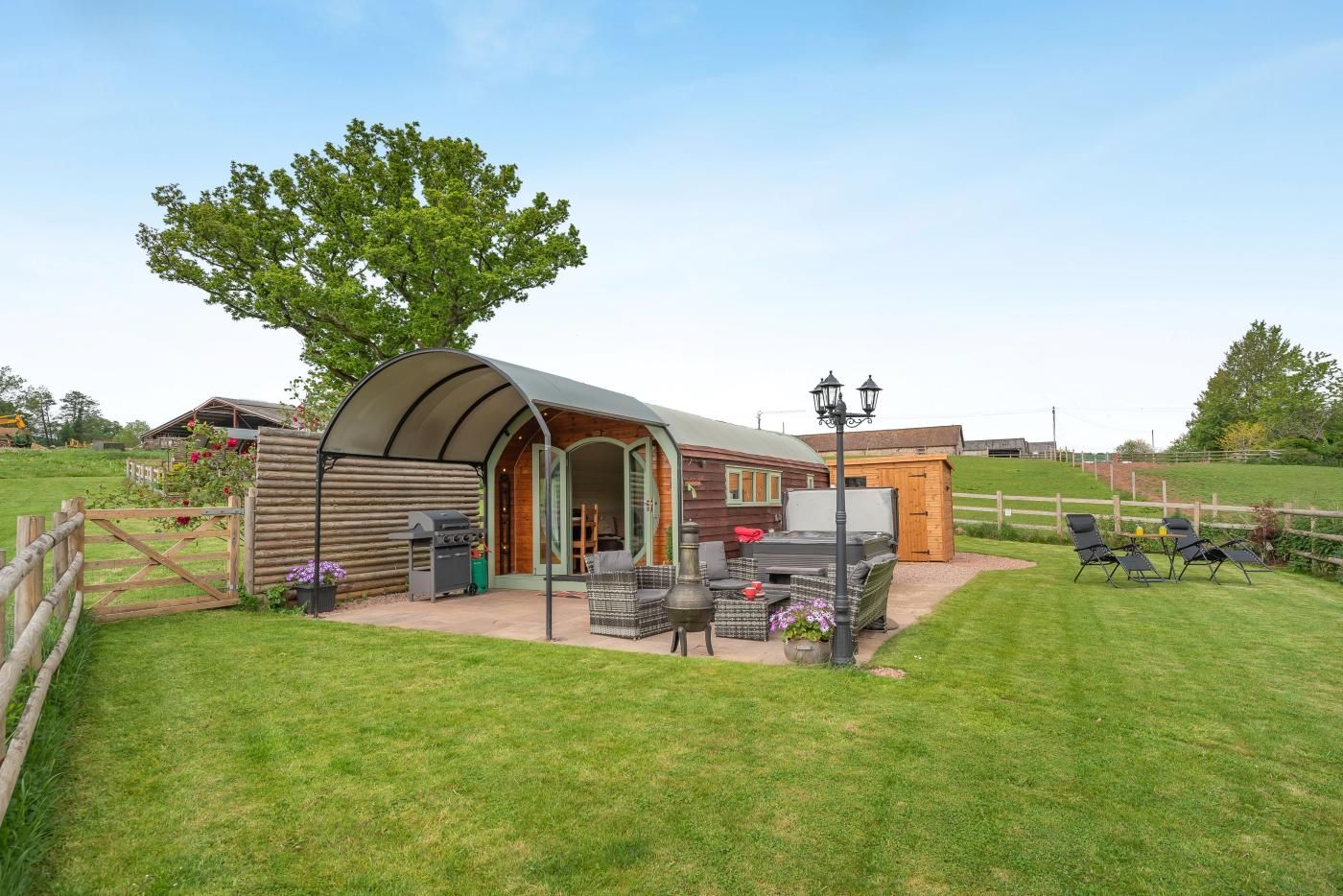 A rustic outdoor seating area with a covered structure, a grill, and a small wooden building.