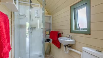 Een badkamer met een douchecabine van glas, een witte wastafel en een raam met groene omlijsting.