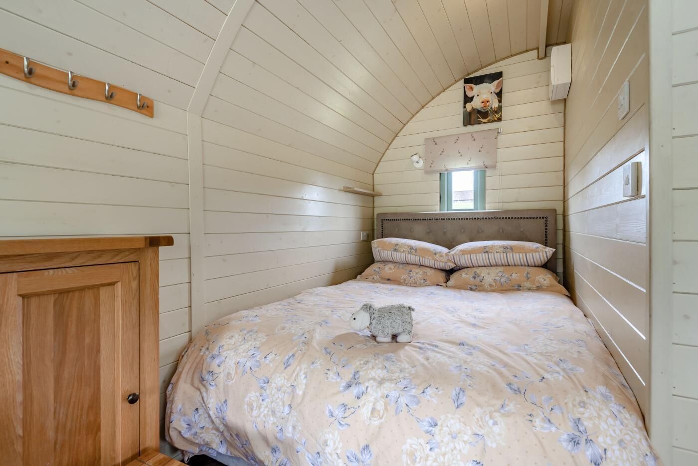 Une chambre avec un lit superposé en bois, une armoire en bois, une petite fenêtre et un luminaire fixé au mur.