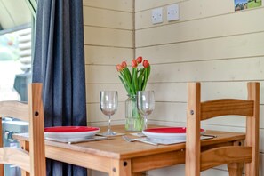 Una mesa de madera con dos copas de vino y un jarrón de tulipanes, frente a una pared con paneles y una cortina.