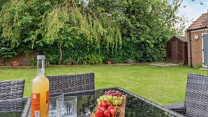 Un espace extérieur aménagé pour les repas, avec des meubles en osier, une bouteille de boisson et un plateau de fruits.