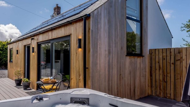 A wooden cabin with a hot tub, a deck, and a large sliding glass door. - 1 Bed in Woolacombe (oc-82341) (Woolacombe)