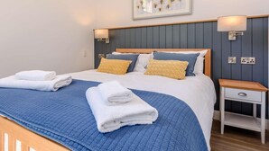 A neatly made bed with blue and white bedding, a wooden headboard, and a bedside table with a lamp. - 1 Bed in Woolacombe (oc-82341) (Woolacombe)