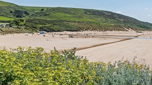 A beach with tents and people, surrounded by green hills. - 1 Bed in Woolacombe (oc-82341) (Woolacombe)