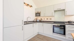 A modern kitchen with white cabinets, a built-in microwave, a stove, and a sink. - 1 Bed in Woolacombe (oc-82341) (Woolacombe)