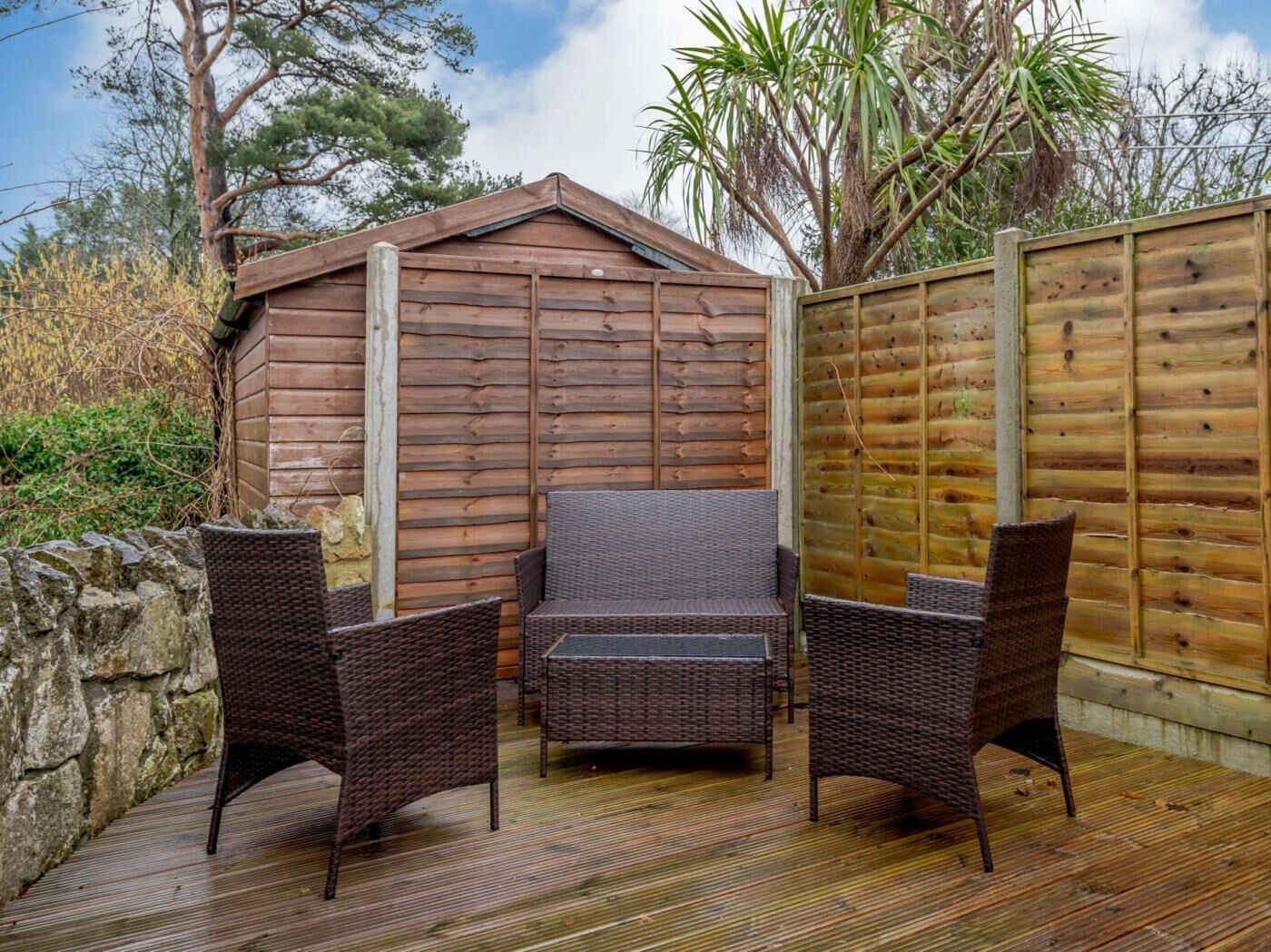 A wooden deck with wicker furniture, a stone wall, and a wooden fence.