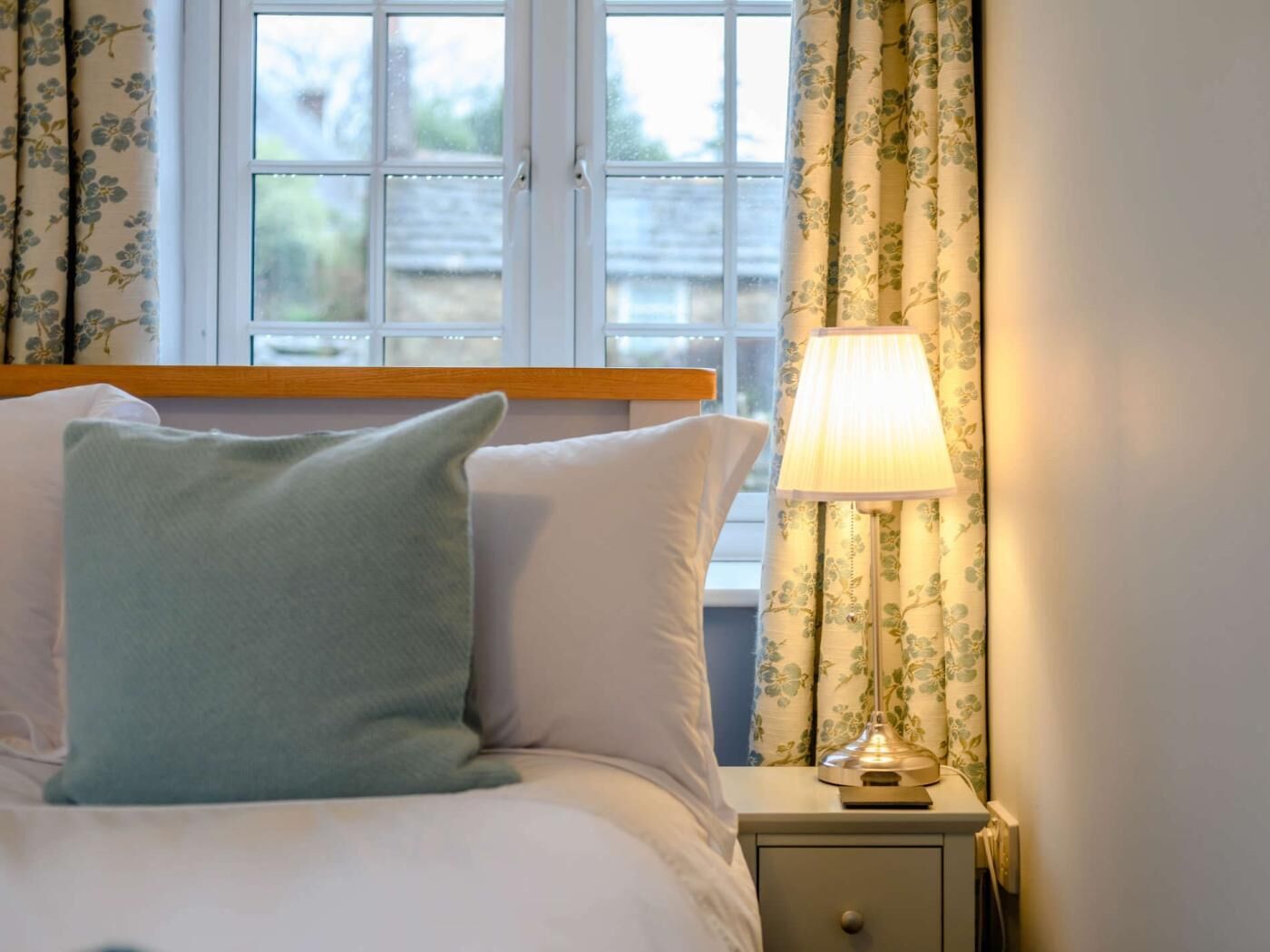 Una cama con almohadas, una lámpara de noche y una ventana con cortinas.