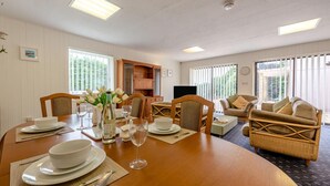 A dining area with a wooden table set for a meal, surrounded by wicker chairs, and a sofa with cushions. - 3 Bed in Pembroke (oc-fb316) (Lamphey)