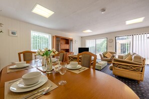 Ein Essbereich mit einem Holztisch, gedeckt für eine Mahlzeit, umgeben von Korbstühlen und einer Couch mit Kissen.