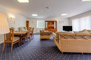 Ein Zimmer mit Esstisch, Stühlen, einer Couch, einem Fernseher und einem Fenster mit Jalousien.