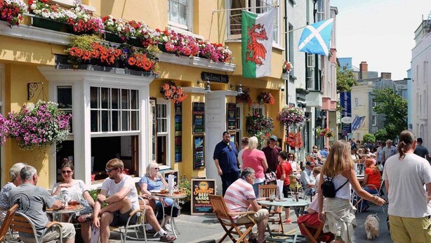 A street with outdoor seating, a pub with a sign for 'The Sunniest Beef Garden,' and flags. - 3 Bed in Pembroke (oc-fb316) (Lamphey)