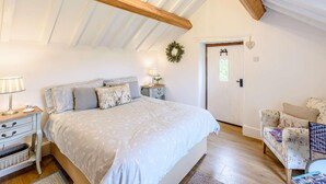 Ein Schlafzimmer mit Bett, Nachttischen, einem Schminktisch, einem Sessel, einer Tür und einer Kandelaber.