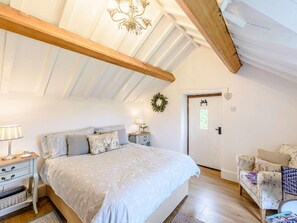 Ein Schlafzimmer mit Bett, Nachttischen, einem Schminktisch, einem Sessel, einer Tür und einer Kandelaber.