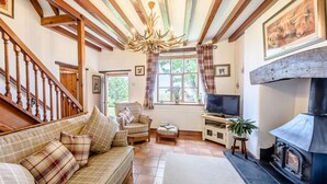 Ein gemütliches Wohnzimmer mit einer Couch, Fernseher, Kamin und Holzbalken an der Decke.