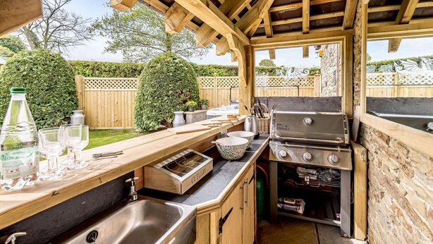 Eine Außenküche mit Grill, Spüle und Holzausziehtisch.