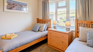 Quarto com duas camas de solteiro, cómoda de madeira, janela com cortinas e um quadro na parede.