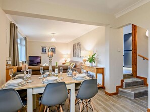 Ein Essbereich mit Tisch für vier Personen, einer Couch, einem Fernseher und einer Treppe, die in eine obere Etage führt.