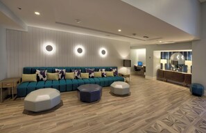 Ein modernes Wohnzimmer mit einem türkisgrünen Sofa, drei weißen Hocker und einem Holzboden im Fischgrätmuster.