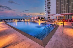 Ein Schwimmbecken mit Liegestühlen und Sonnenschirmen, umgeben von einem Hochhaus.