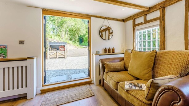 A cozy living room with a brown leather sofa, a wooden-framed ceiling, and a large sliding glass door leading to an outdoor area. - 1 Bed in Ashford (oc-82527) (Biddenden)