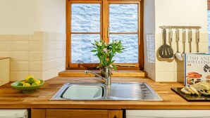 Una cocina con encimera de madera, un lavamanos de acero inoxidable, una ventana con vistas al mar y un libro titulado 'Pescados y Mariscos' en la pared.