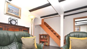 Una sala de estar con sofás de cuero verde, una escalera de madera, un reloj y una estantería.