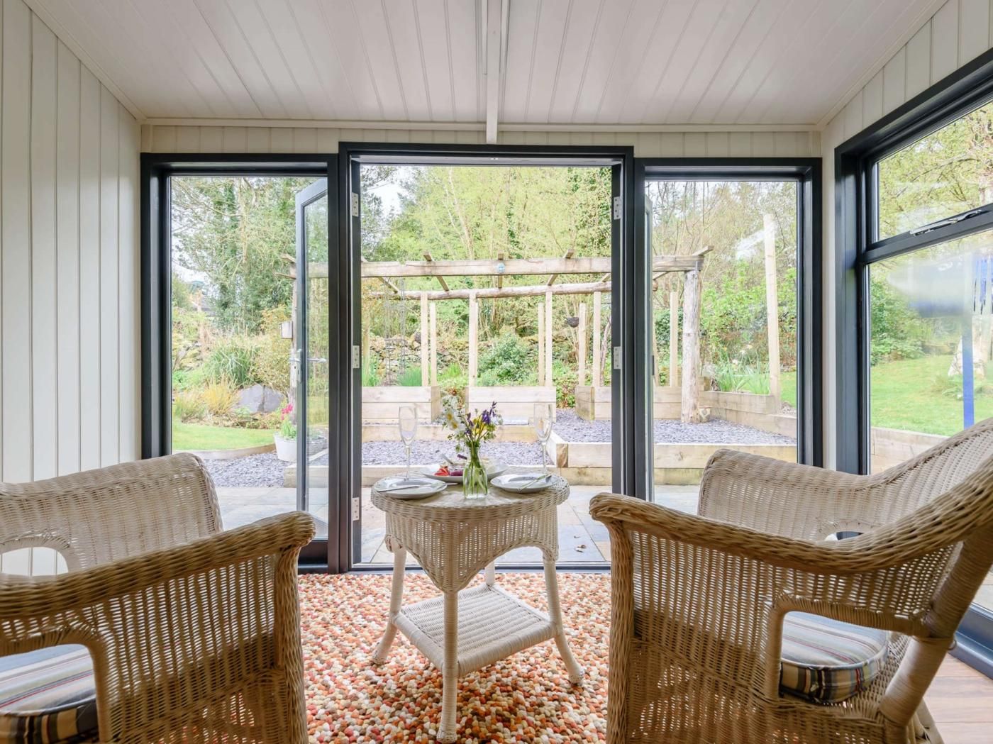 A conservatory with wicker furniture, a glass table, and a view of a garden.