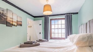 Un dormitorio con cama, ventana con cortinas, una puerta y una lámpara colgante.