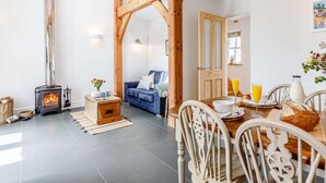 Een gezellige woonkamer met een open haard, een eethoek met een tafel en stoelen, en een blauwe bank.