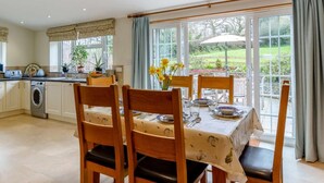 Una cocina con lavadora, mesa de comedor con sillas y vistas a un jardín a través de ventanas amplias.