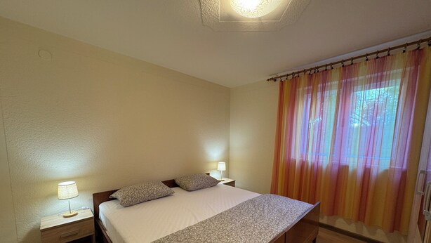 Ein Schlafzimmer mit einem Bett, zwei Nachttischen, einem Fenster mit Vorhängen und Holzboden.