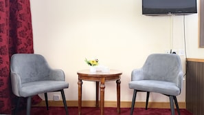 A room with two grey armchairs, a small wooden table with a vase of flowers, and a flat-screen TV mounted on the wall. - Elite Jonrad Hotel (Dubai)