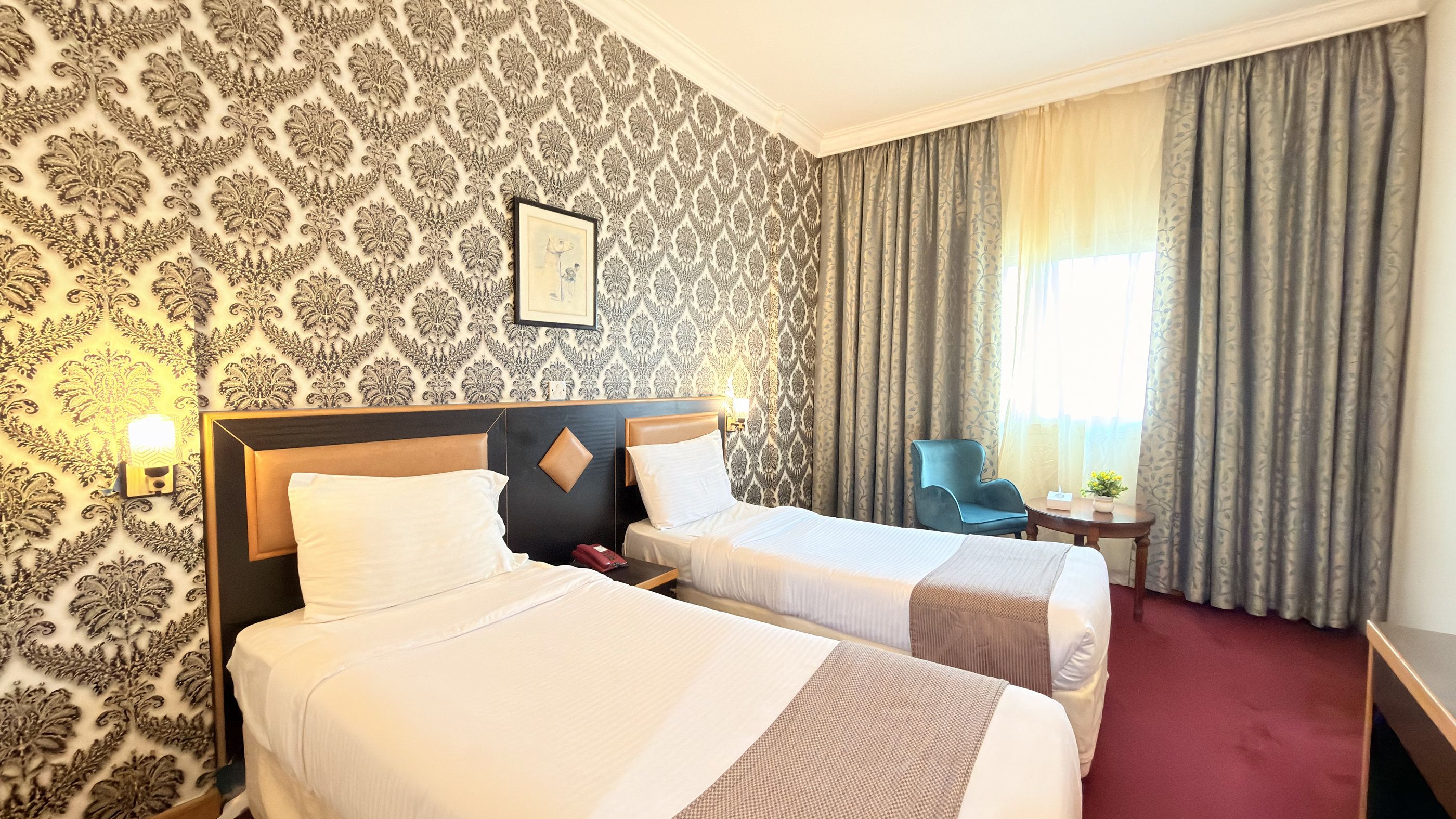 Une chambre d’hôtel avec deux lits, une table de chevet, une chaise, une petite table et une fenêtre avec des rideaux.