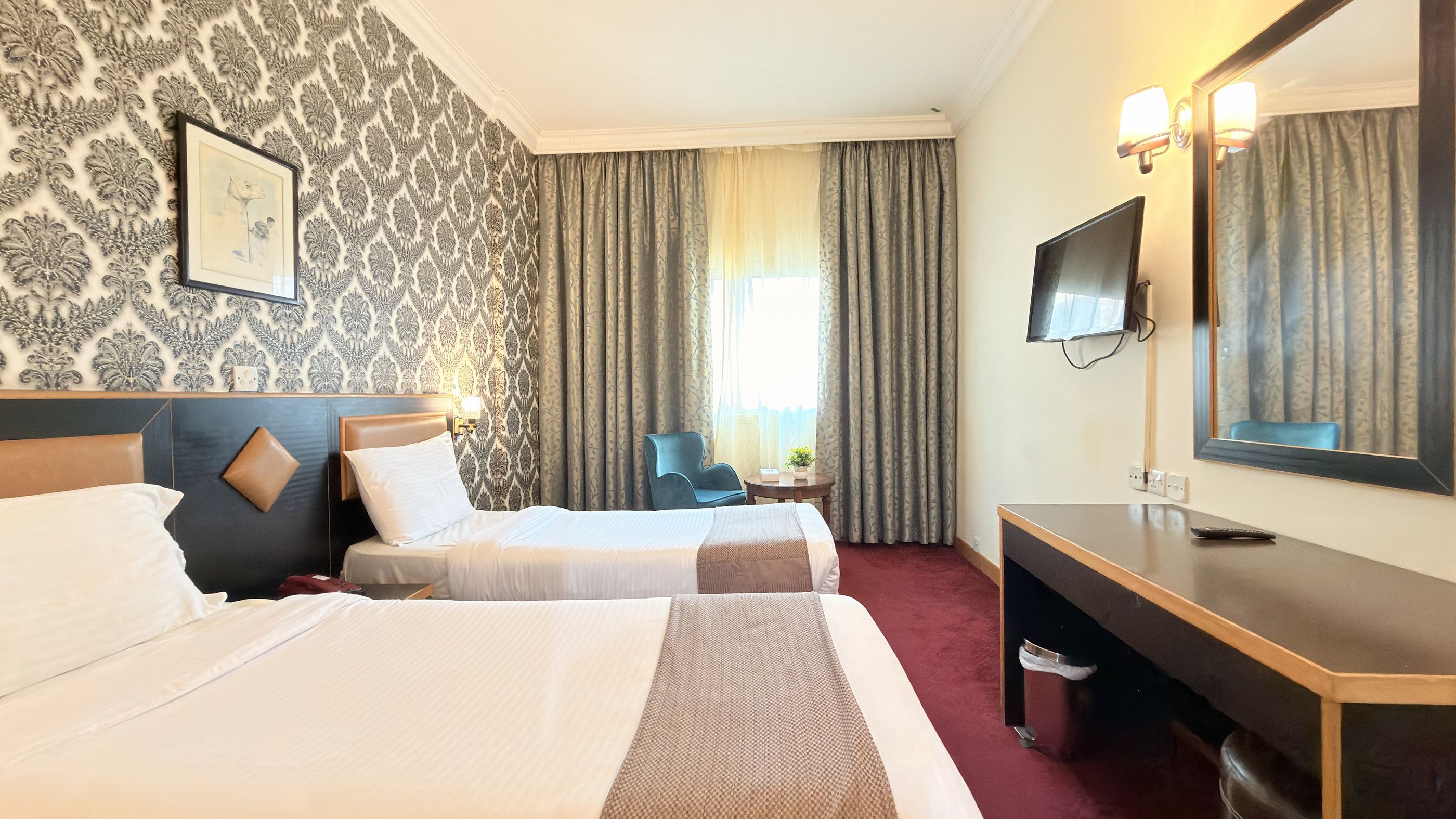 Ein Hotelzimmer mit zwei Betten, einem Schreibtisch, einem Stuhl, einem Fernseher und einem Fenster mit Vorhängen.