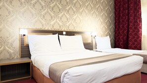 A hotel room with a double bed, a nightstand, a lamp, and a patterned wallpaper. - Elite Jonrad Hotel (Dubai)