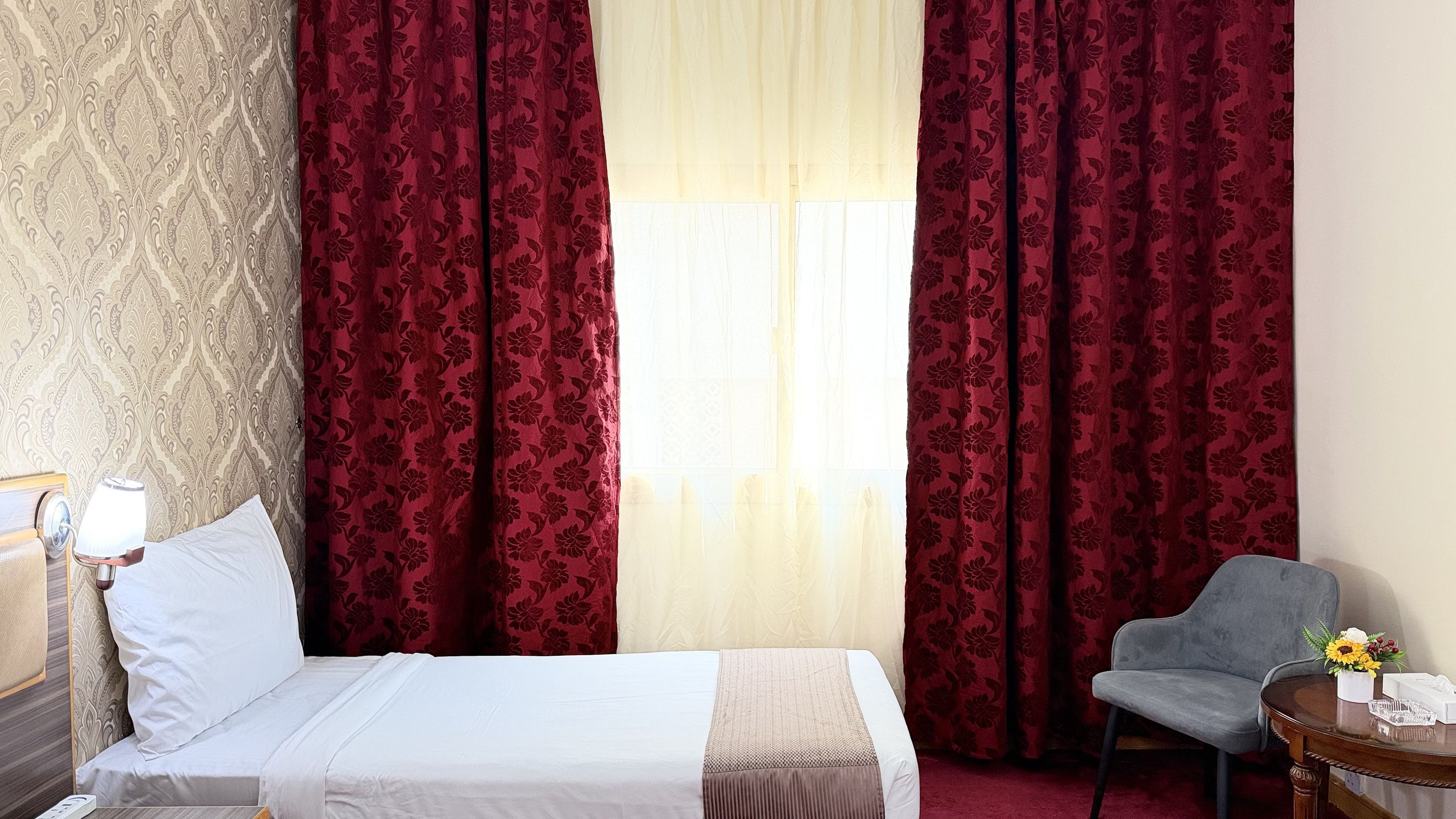 A hotel room with a bed, a chair, a lamp, and curtains.