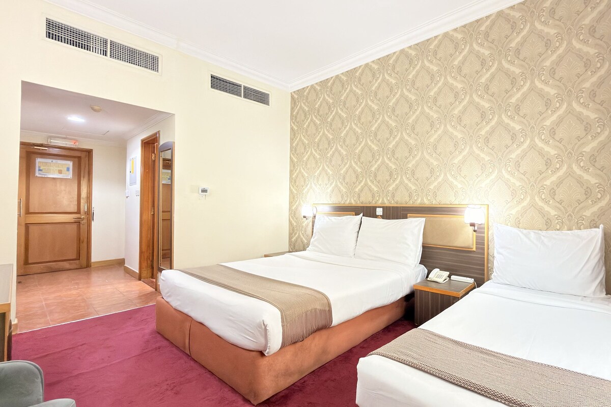 Habitación de hotel con dos camas, un cabecero de madera, una mesita de noche con teléfono y una cortina roja.