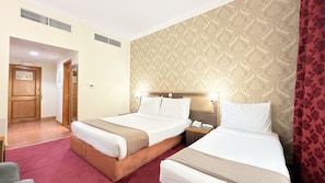 A hotel room with two beds, a wooden headboard, a nightstand with a phone, and a red curtain. - Elite Jonrad Hotel (Dubai)