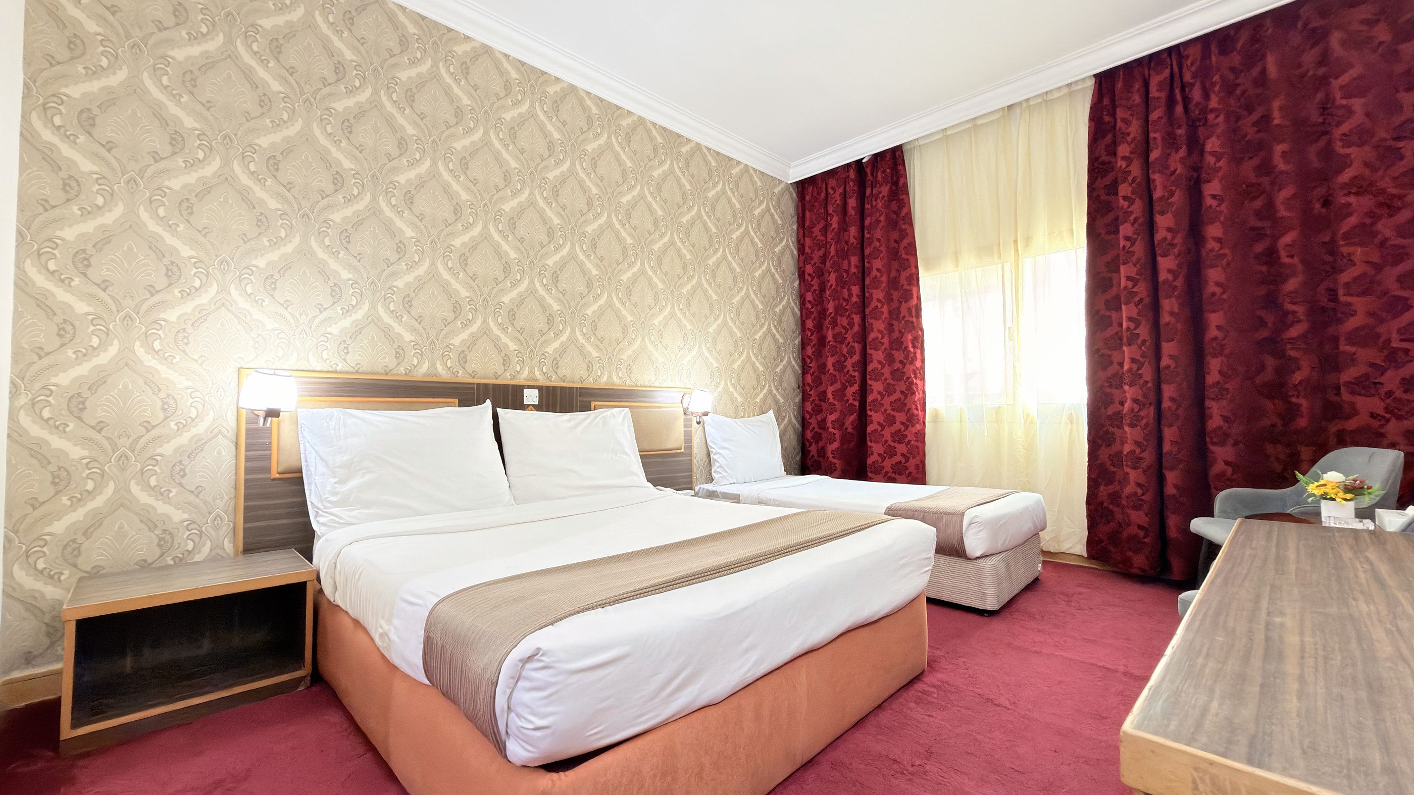 A hotel room with a large bed, a smaller bed, a desk, and a chair.