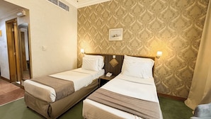 A hotel room with two single beds, a small bedside table with a lamp, a telephone, and a framed picture on the wall. - Elite Jonrad Hotel (Dubai)