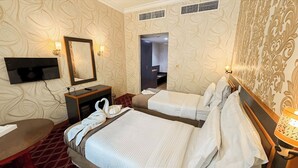 A hotel room with two beds, a TV mounted on the wall, a desk, and a mirror. - Elite Jonrad Hotel (Dubai)