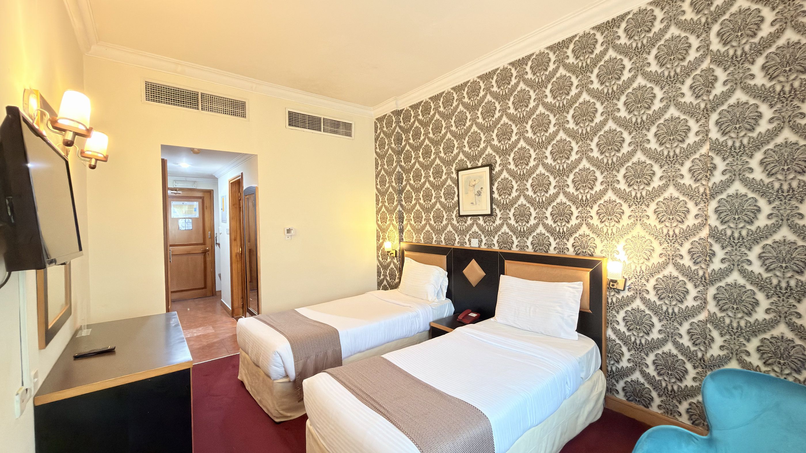 Une chambre d’hôtel avec deux lits, une télévision et un papier peint à motifs.