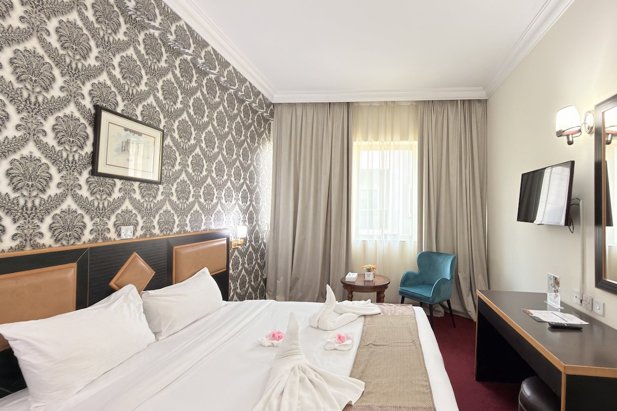 Habitación de hotel con cama, escritorio, silla, espejo y ventana con cortinas.