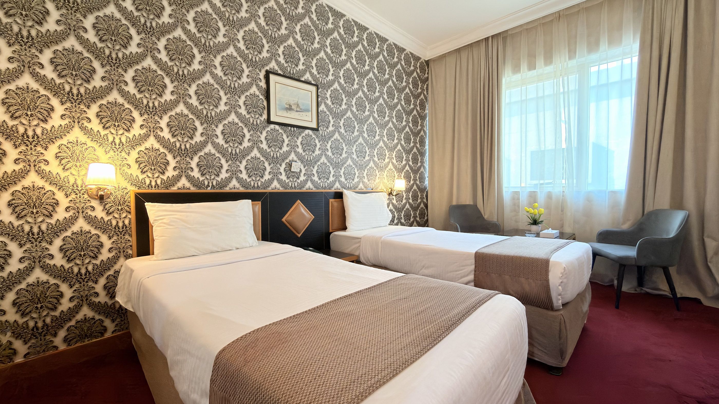 Habitación de hotel con dos camas, un escritorio, una silla, una lámpara y una ventana con cortinas.