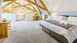 A bedroom with a sloped ceiling, wooden beams, a bed, bedside tables, and a dresser. - 6 Bed in Torrington (oc-81519) (Great Torrington)
