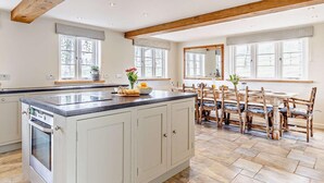 A spacious kitchen with a central island, wooden beams, large windows, and a dining area with wooden chairs. - 4 Bed in Tiverton (oc-82433) (Witheridge)